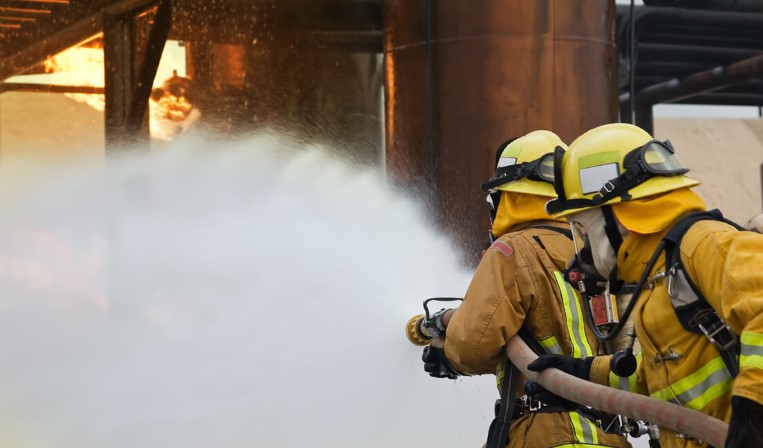 Two firefighters spraying water at a fire with a hose