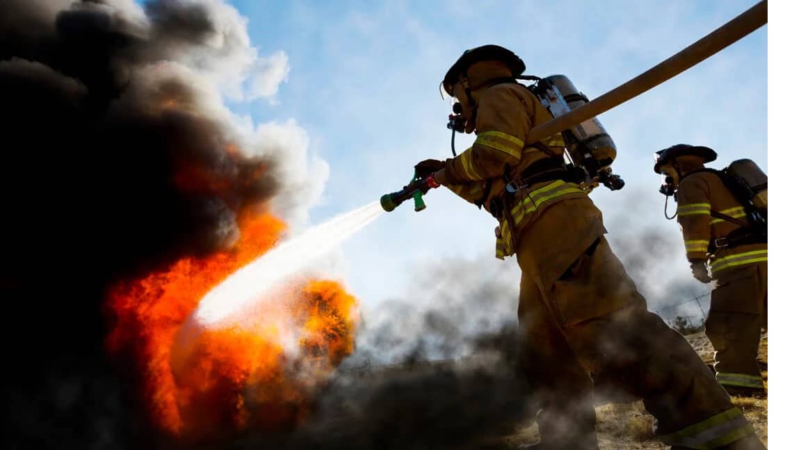 Fighting Fire and Maximizing Efficiency with Water One® Services. Image depicts two firefighters. One is spraying water at a fire with a hose.