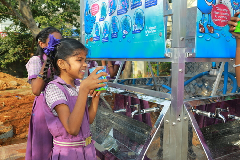Girl holding a cup of water next to an outdoor sink